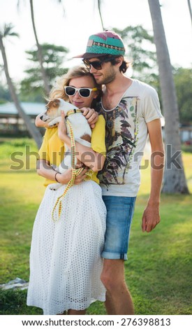 Young family in love on the beach in summer sunny evening with little dog.Summer mood,summer portrait of young couple in love,wearing sunglasses,hipster couple on island,tropical romance,bright color