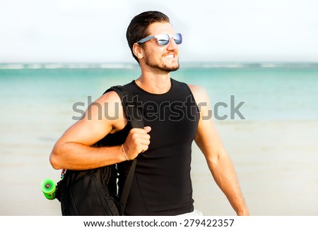 Portrait of bearded man with sunglasses,travel bag optic the ocean.Adventure man hiking wilderness with backpack,outdoor lifestyle extreme vacation.Hipster man with skateboard,summer mans outfit