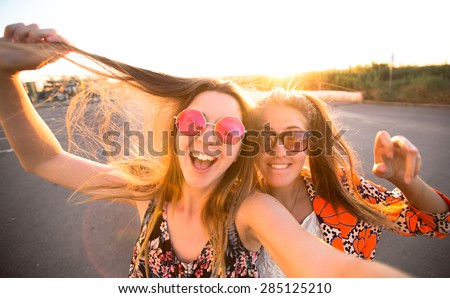 close-up lifestyle portrait of young best friends girls having fun at cool sunset.Travel concept,happy girls make picture together and having fun,laughing and make funny faces on camera,sunshine girls