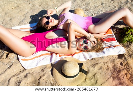 Colorful portrait of cheerful girls laying on the beach in trendy swimsuits,travel concept.Summer fashion toned colors,outdoor fashionable portrait of best friends in the same bikinis,summer warm days