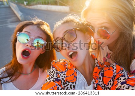 Close-up portrait of group of tree young friends wearing sunglasses,stylish friends,hugging and standing in a row at sunset, spending time with friends.posing on gold sunset,Make self picture