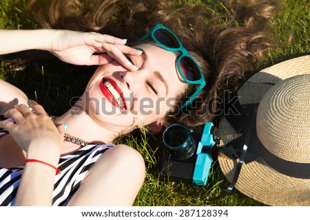Attractive happy curled woman laying on the green ground wear summer dress,crying with happiness.Portrait of Laughing and having fun funny teenage girl.camera,summer straw hat,lifestyle concept