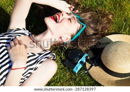 Close up lifestyle portrait of cheerful brunette hipster girl going crazy making funny face and showing her tongue.Laying on the ground and laughing.Bright colors,urban street background.accessories