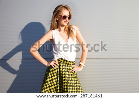 Beautiful young sexy girl with long wavy blonde hair with a bright evening make-up perfect summer tan thin figure dressed in colored summer Skirt and white shirt,neon heels,holding glamorous glasses