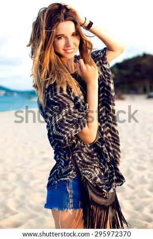 Summer lifestyle fashion portrait of young woman in stylish outfit,walking near ocean, positive mood,vintage toned colors.Caucasian female wearing sunglasses looking away,outdoors on summer vacation.