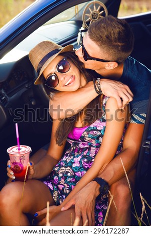 Young couple on road trip. Young couple sitting on the hood of their car with man answering a phone call and woman sitting by. Car is parked alongside coastal seashore with bright sunlight. sunshine