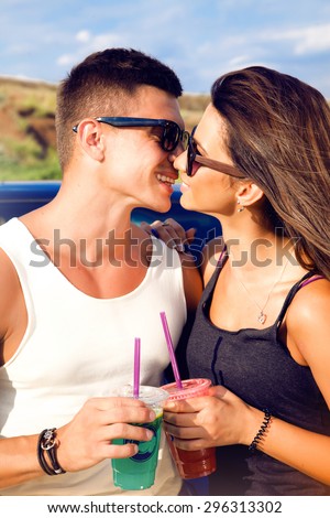 Woman kissing her boyfriend driving a car.Lovely young couple on road trip.Affectionate caucasian couple enjoying road trip,cocktail, smoozy drink, denim jacket,smiling,fashion,teen,cool accessories