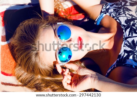 Beautiful blonde young woman wearing sunglasses,shorts,green top and handbag, laying on the beach,red lips,fresh face,model face,tan woman,sensual woman,long hair,reflection sunglasses,mirrored glass