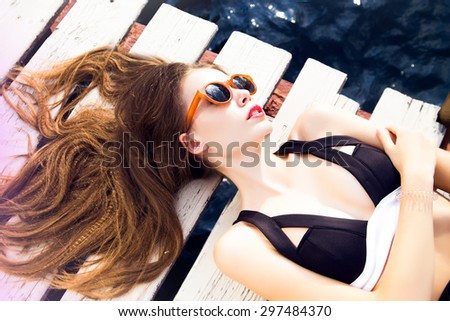 Young pretty fashion woman body posing in summer in pool with clear water lying on mattress in black bikini and having fun,carefree woman at sunset on the beach.Outdoors lifestyle portrait girl,toned