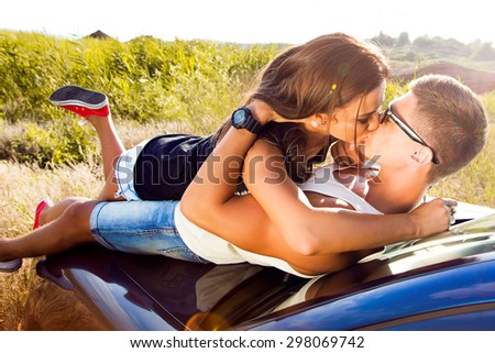 Cars - couple driving in new car smiling happy looking at camera and  kissing.Young people on road trip drive in car.Outdoor sensual couple laying on the car enjoy their trip together,casual outfit