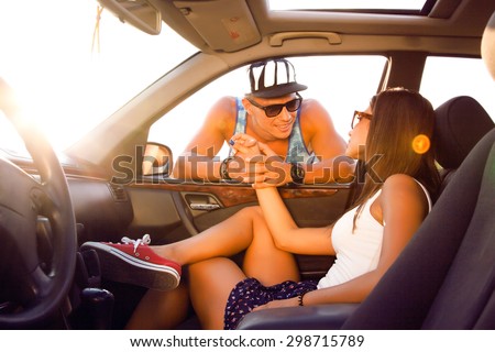 Young couple looking into each other's eyes.young friends,sitting on their car.cheerful friends enjoying road trip in their convertible while handsome man adjusting his sunglasses and smiling,roadtrip