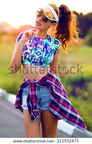 Lifestyle portrait of trendy woman in hipster outfit.Hiker Outdoor,fashion woman,crop top.Neon hat,cap,Sportive style,fall fashion,autumn look,crazy mood,stylish girl posing on sunset,sunshine woman