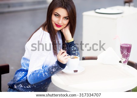 Close up image of woman holding cup of tasty cappuccino,bright manicure,gold watches and bracelets,lifestyle bright image of woman drinking her morning coffee on the street cafe,flirting,autumn colors
