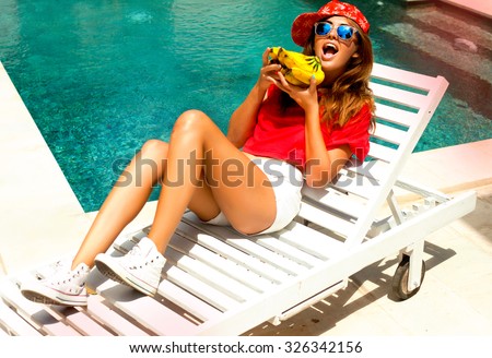 Young crazy teen girl laying and relaxed near pool at summer holiday nice hot day,crazy of her bananas,crop top,white shirts,swagger cap,listening music at big headphones.toned body,diet conception