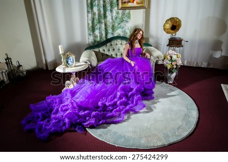 Woman in a luxury, long purple dress sitting on the couch