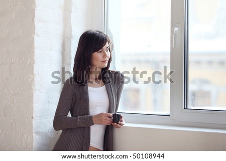 The young beautiful girl is by the window and looks out of the window