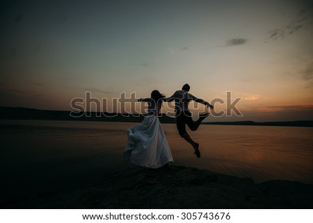 Young couple bride and groom jump into the water at sunset. Newlyweds walking near the river