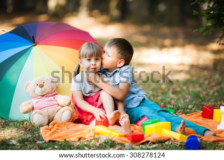 boy and girl playing on the meadow in the park. Brother sister kisses. Children sit on the blanket and playing with colorful toys