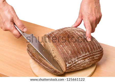 Human hand with a knife cut rye bread on a cutting board