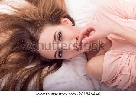 The beautiful young girl in a pink jacket smiles, holding a hand at a mouth, lying on a bed