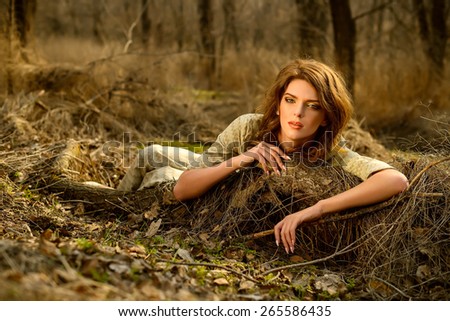 the beautiful red-haired girl in a green dress lies, having leaned on a log in the spring wood, hands lie on a log