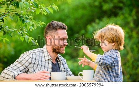 Dad and boy eat and feed each other outdoors. Ways to develop healthy eating habits. Feed your baby. Natural nutrition concept. Feeding son natural foods. Stage of development. Feed son solids