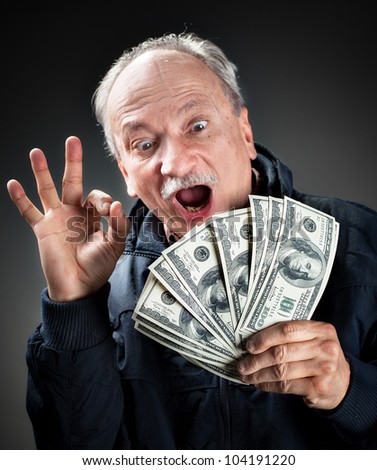 Happy elderly man showing fan of money and sign OK with fingers. Focus on money.  Softly blurred face