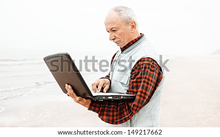 Old man on beach working with notebook on a foggy day