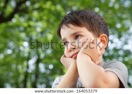 Sad little boy looking at something against blurred natural background