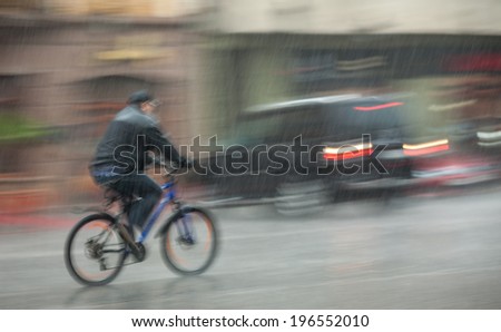Rainfall in the city. Wet cyclist rides through the streets on a rainy day. Intentional motion blur