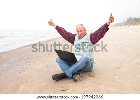 Happy old man on the beach with a laptop on a foggy day