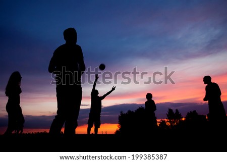 Night scene. Silhouettes of young people playing with a ball on the sunset sky background