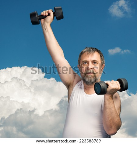 Elderly man exercising with dumbbells against the blue sky with white clouds