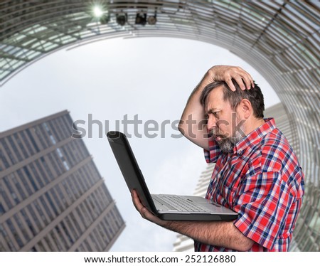 Problems with computer. Middle aged stressed businessman working on laptop against urban background