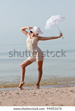 Woman in a striped retro bathing suit with a white umbrella posing against the sea