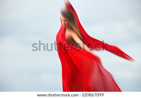 Soft focus image of blurred woman with red fabric posing against sky background
