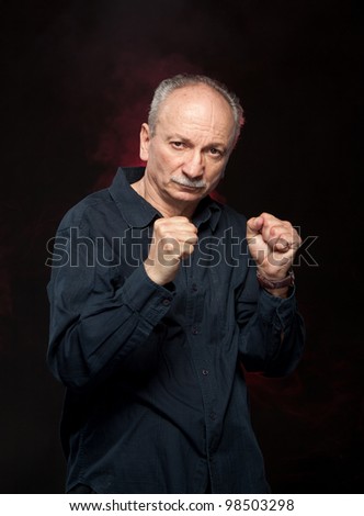 Mature man in boxer pose with raised fists on black background