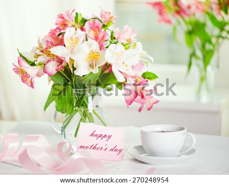 Beautiful bouquet of alstroemeria in a vase with water,  white cup of tea, greeting card with the inscription \