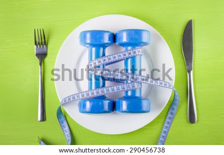 The concept of a healthy lifestyle, diet, sports, weight loss, anti obesity, exercise, healthy diet.  Centimeter and  dumbbells on a plate, knife and fork, on the table, top view, closeup