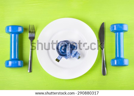 The concept of a healthy lifestyle, diet, sports, weight loss, anti-obesity, exercise, healthy diet.  Centimeter on a plate, knife, dumbbells and fork, top view, closeup