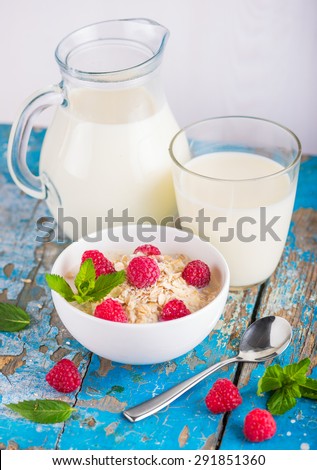 Oat flakes with milk and raspberries for breakfast, glass with milk, jar, spoon,  fresh mint on an old wooden blue background, the concept of a healthy diet, weight loss
