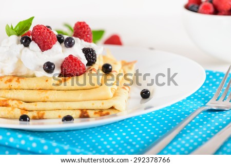 Delicious sweet crepes decorated air-cream and ripe berries, raspberries, blackberries and blueberries on a white plate, bright blue polka dot napkin. Tasty breakfast.