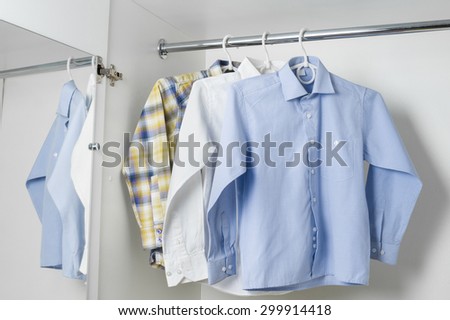 white, blue and checkered clean ironed men\'s shirts hanging on hangers in the white wardrobe