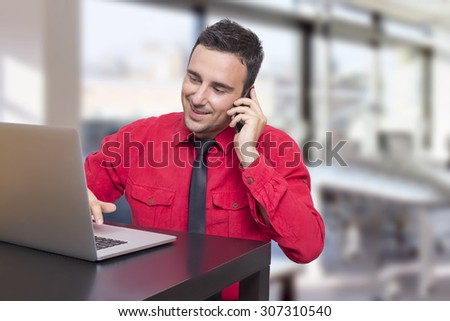 Worker smiling in the office in red shirt in front of his laptop