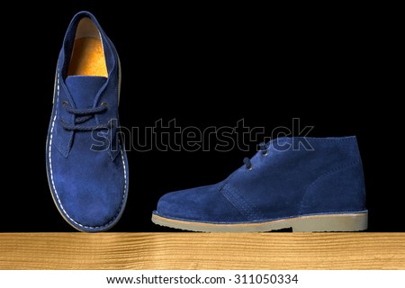 blue suede boots on a wooden shelf over a black background