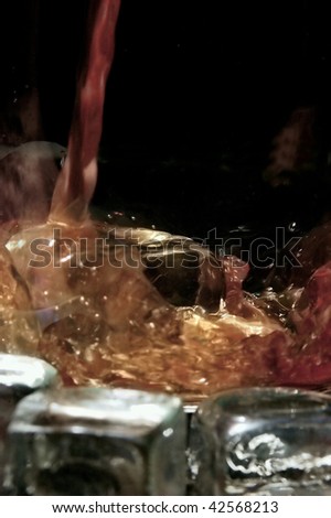 Whiskey flows into a glass with ice cubes to the left against black background in the portrait format as a close-up.