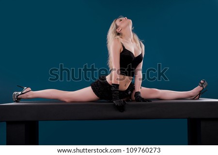 Pretty flexible dancer woman sit on twine and stretching on a blue background