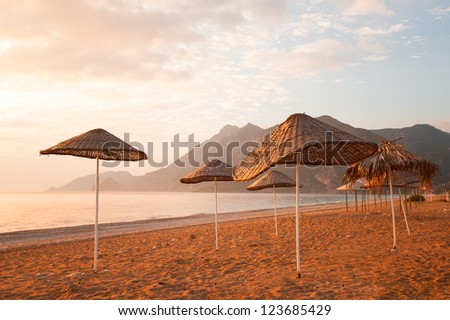 Beach umbrellas at sunset in the Mediterranean Sea Sea and mountains in the background.