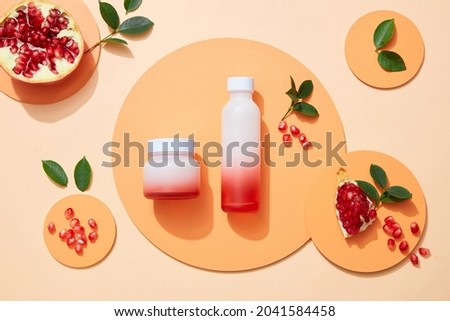 Blank lable Cosmetic set for skin care with pomegranate extract. Whole pomegranate and pomegranate seeds, leaves on podium circle on color background. Topview
