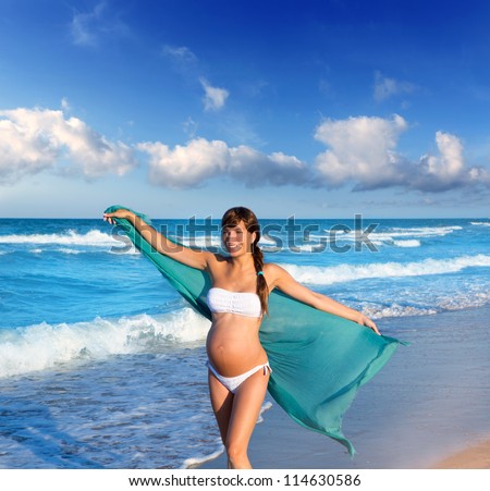 Beautiful pregnant woman walking on blue beach in summer with blowing wind handkerchief